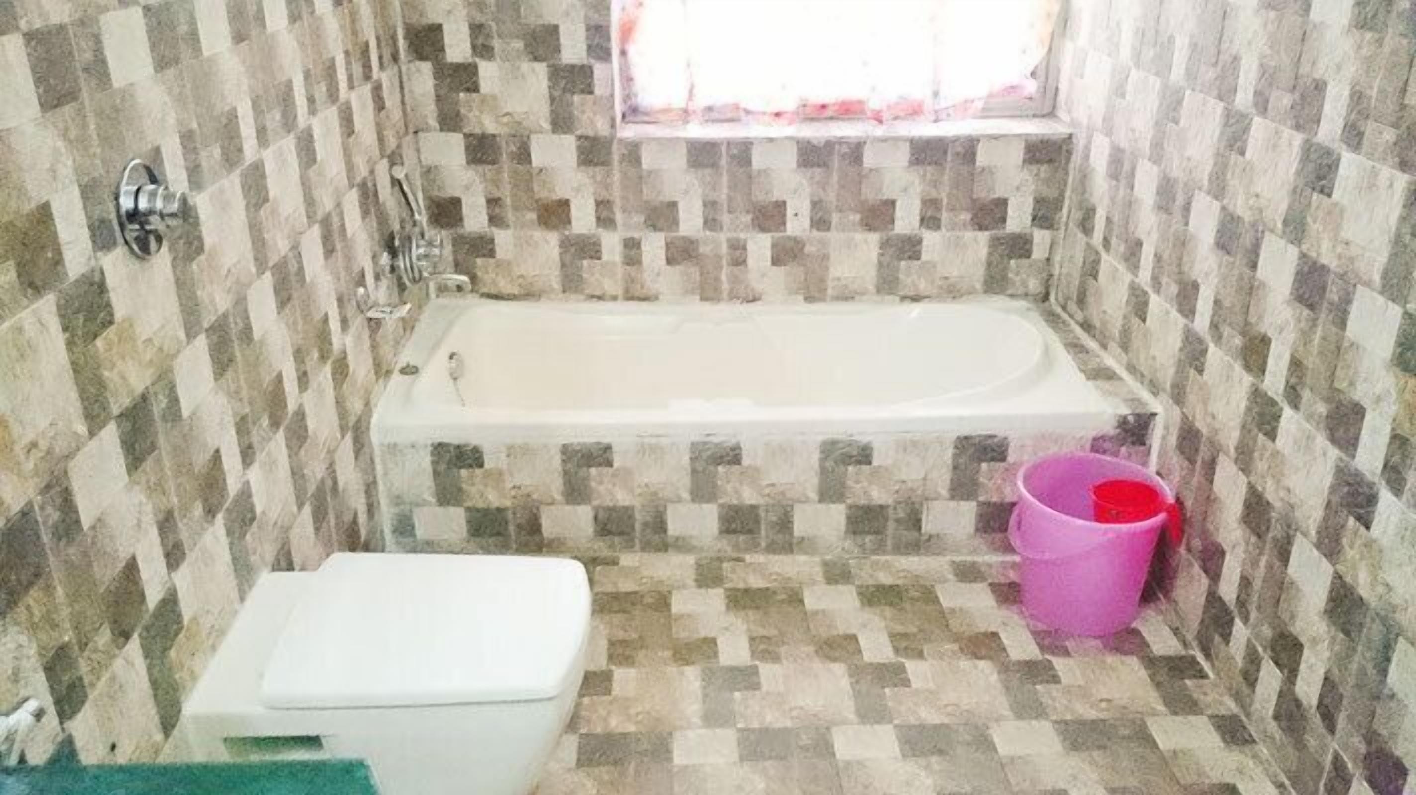 Un baño pequeño con bañera, inodoro y un balde rosa.
