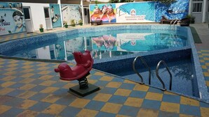 A swimming pool with a checkered floor, a red children's play structure, and a mural advertising the Mahamaya Palace Swimming Pool.