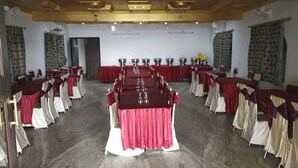 A banquet hall with a long table set for a formal event, surrounded by chairs with red and white drapery.