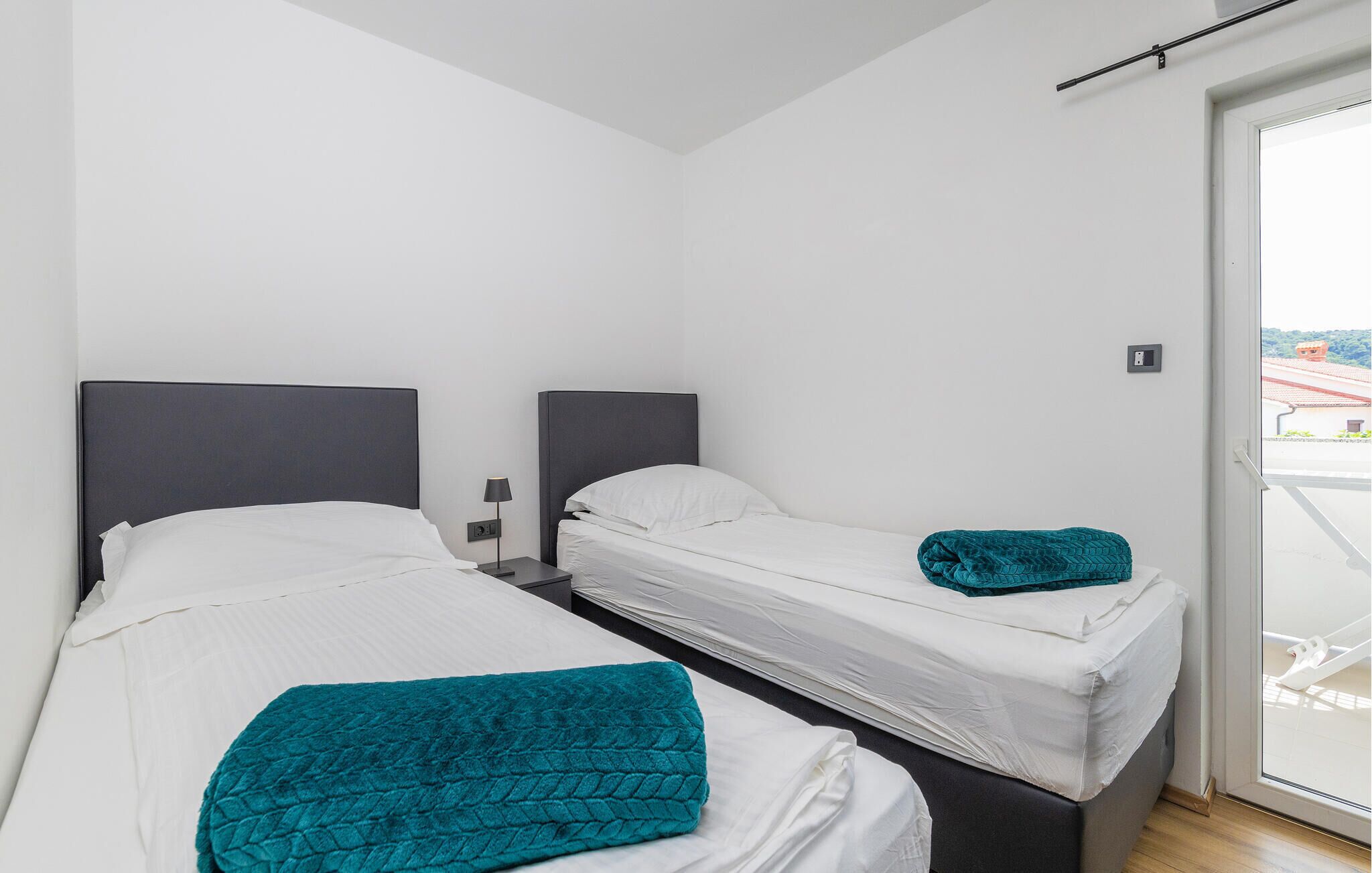 A modern hotel room with two single beds, white linens, and teal throw pillows.