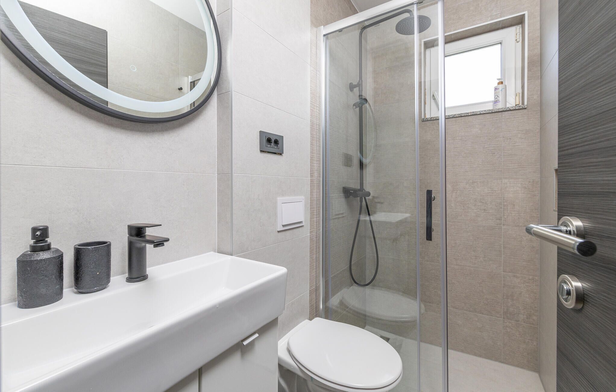 A modern bathroom with a glass shower enclosure, a white sink with a mirror, and a toilet.