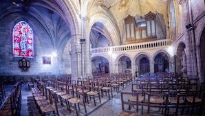 A church interior with rows of wooden pews, a large stained glass window, and a pipe organ. - Au Relais Saint Maurice (Chinon)