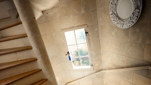 A spiral staircase with wooden steps leading upwards, a window with a view of greenery, and a decorative plate on the wall. - Au Relais Saint Maurice (Chinon)