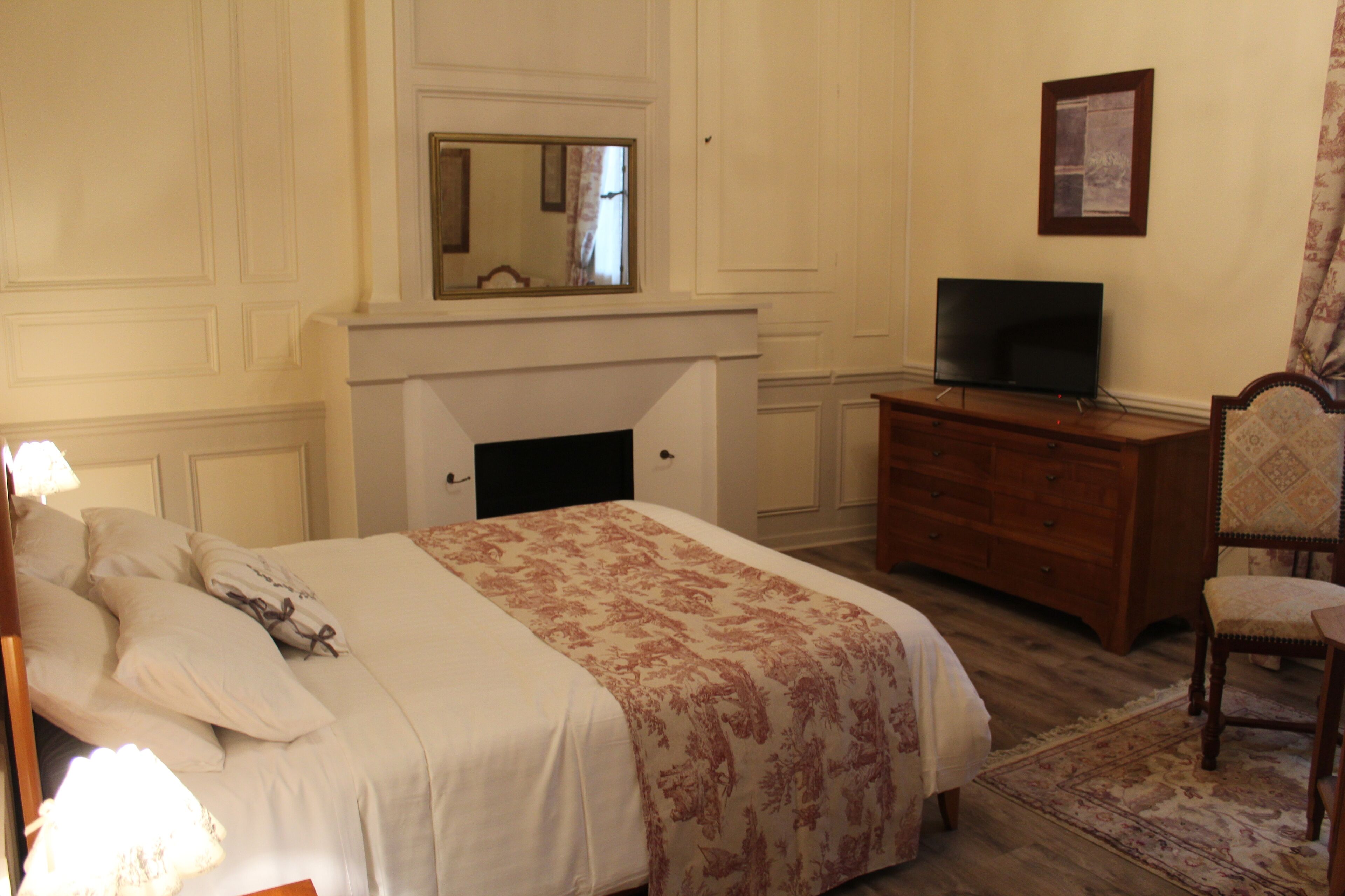 A bedroom with a bed, a dresser, a television, and a fireplace.