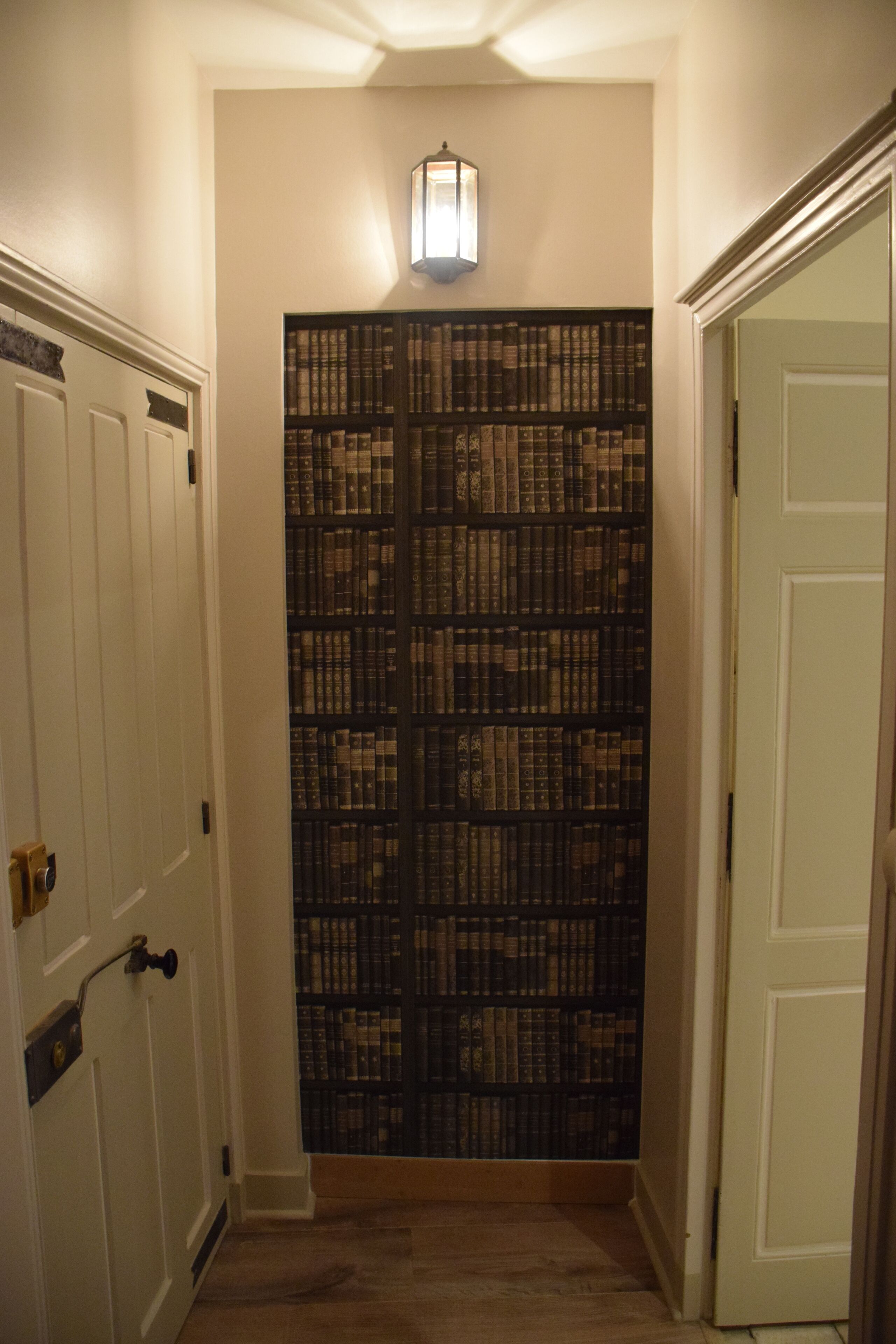A hallway with a bookshelf filled with books, a door with a brass handle, and a light fixture above the bookshelf.