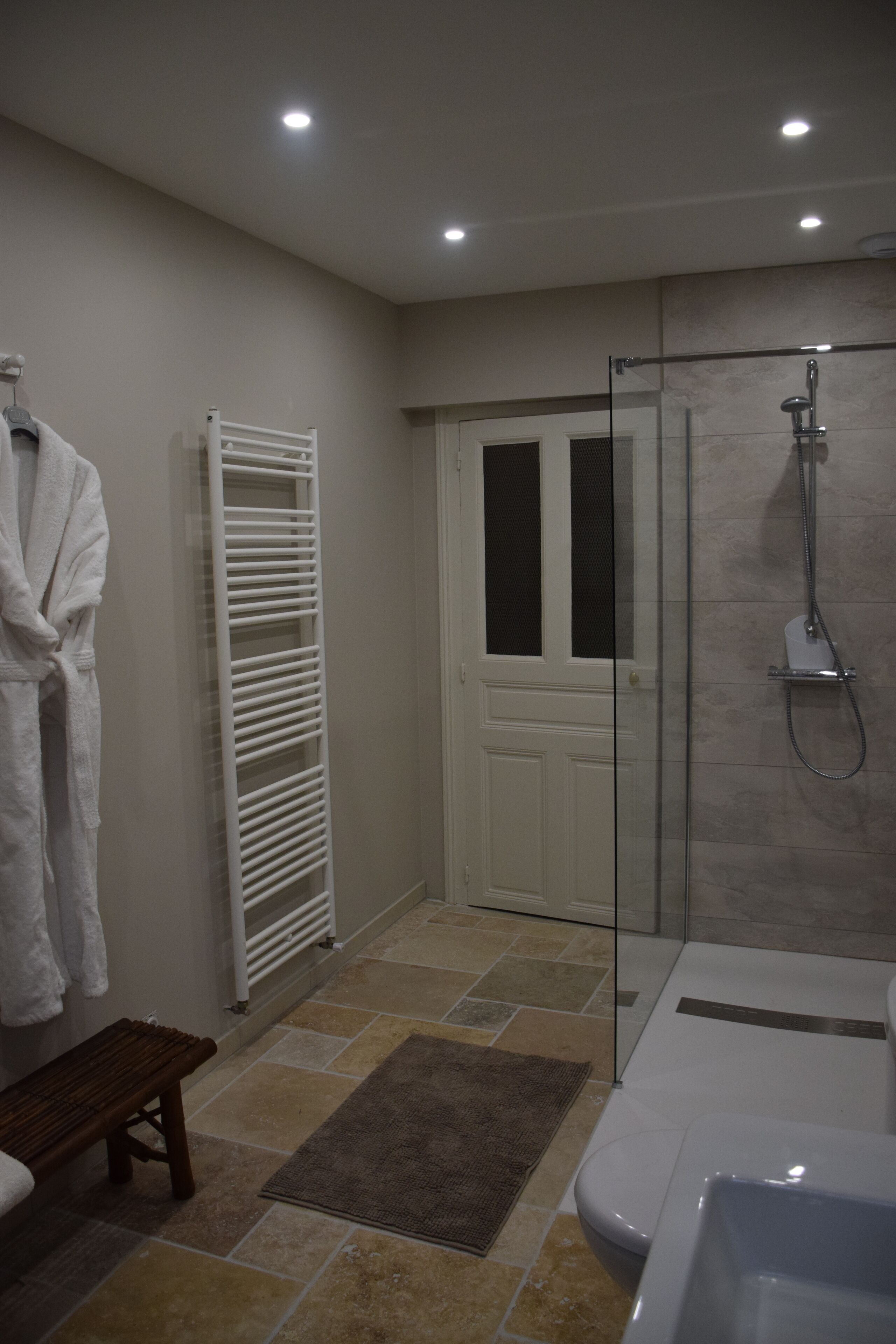 Ein modernes Badezimmer mit einer Duschkabine aus Glas, einer weißen Badewanne und einem Handtuchhalter mit einem weißen Bademantel.