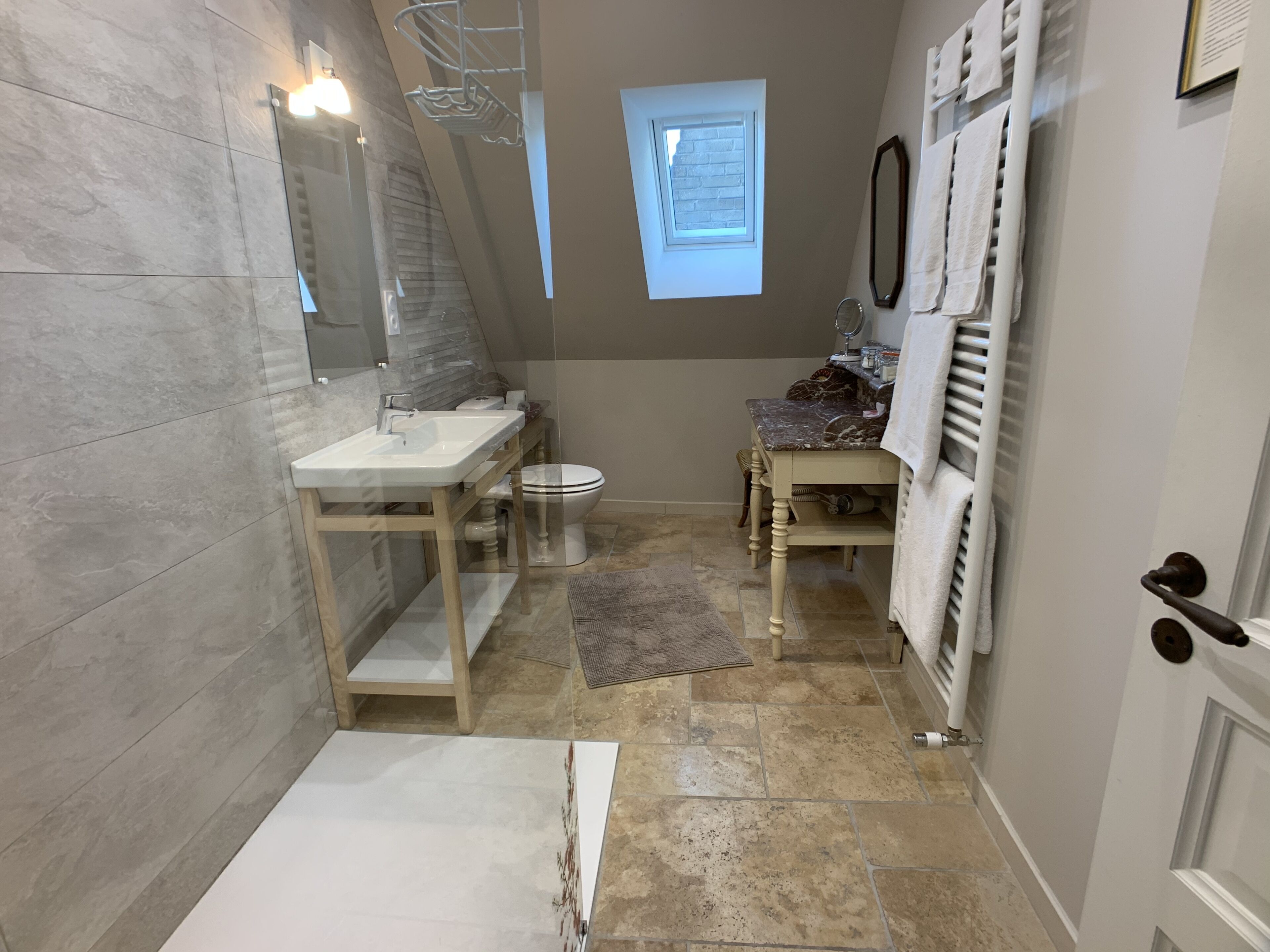 Un bagno con doccia, lavandino e WC. Si vede una finestra sopra il WC e un porta asciugamani sulla parete.