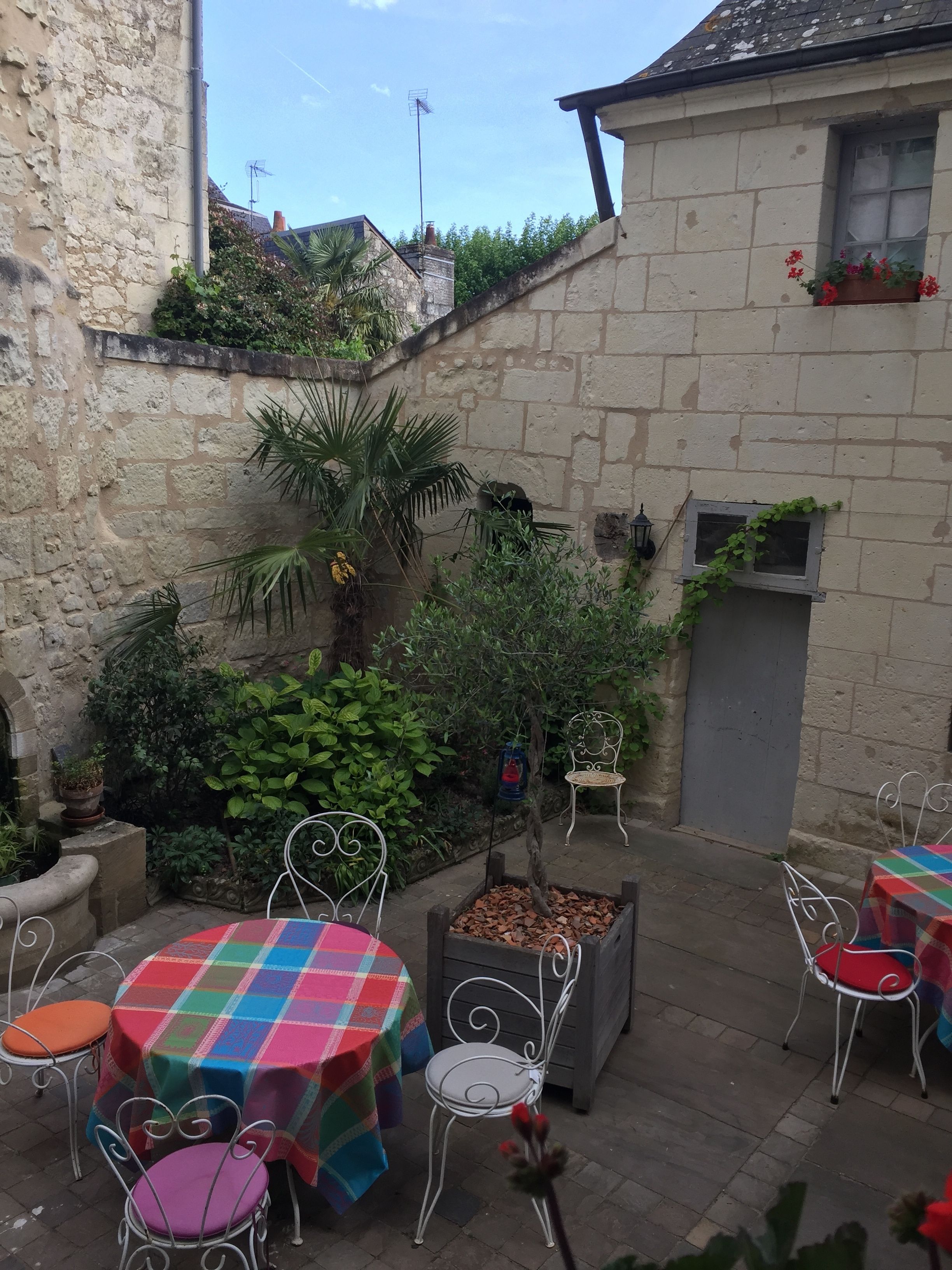 An outdoor patio area with stone walls, potted plants, and metal chairs and tables.