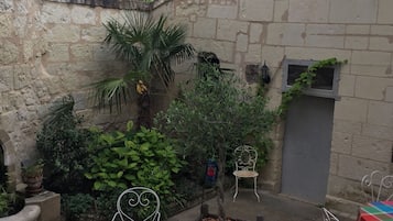 An outdoor patio area with stone walls, potted plants, and metal chairs and tables.