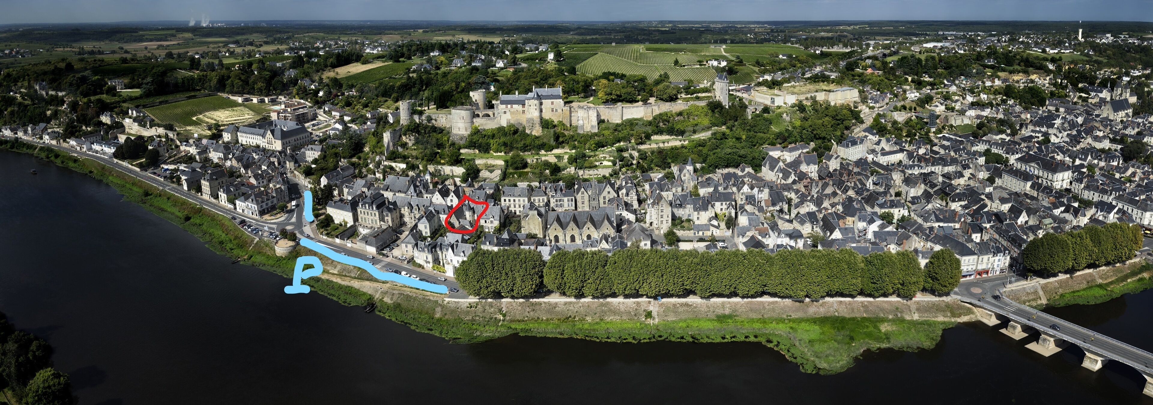 An aerial view of a historic town with a prominent castle, a river, and a bridge.