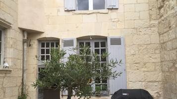 Une cour avec un arbre, des sièges extérieurs et un barbecue couvert.