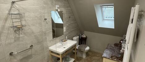 A modern bathroom with a glass shower enclosure, a vanity with a mirror, a toilet, and a small window.