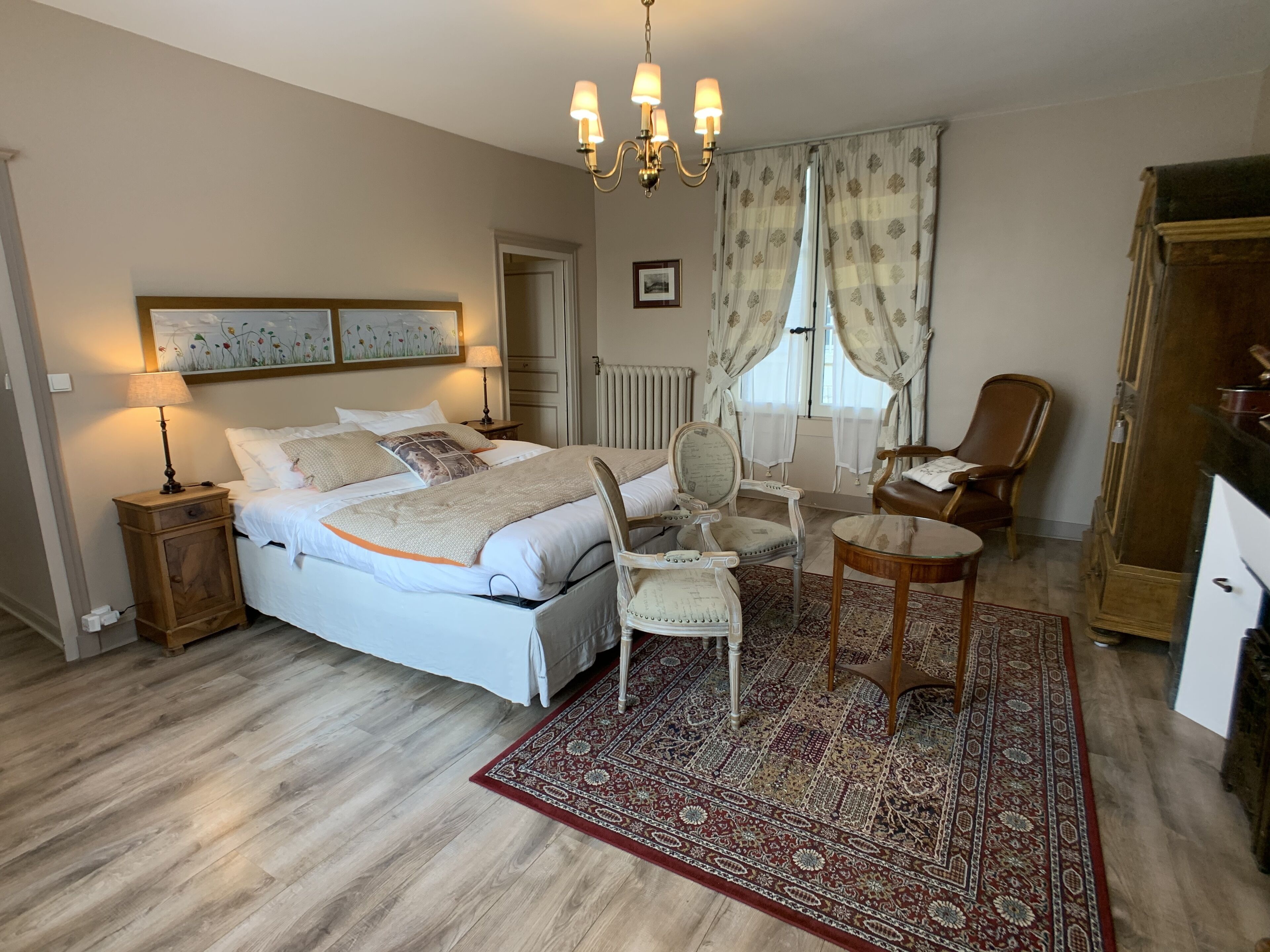 Une chambre à coucher avec un grand lit, une table de chevet en bois, une chaise, une petite table et un lustre.