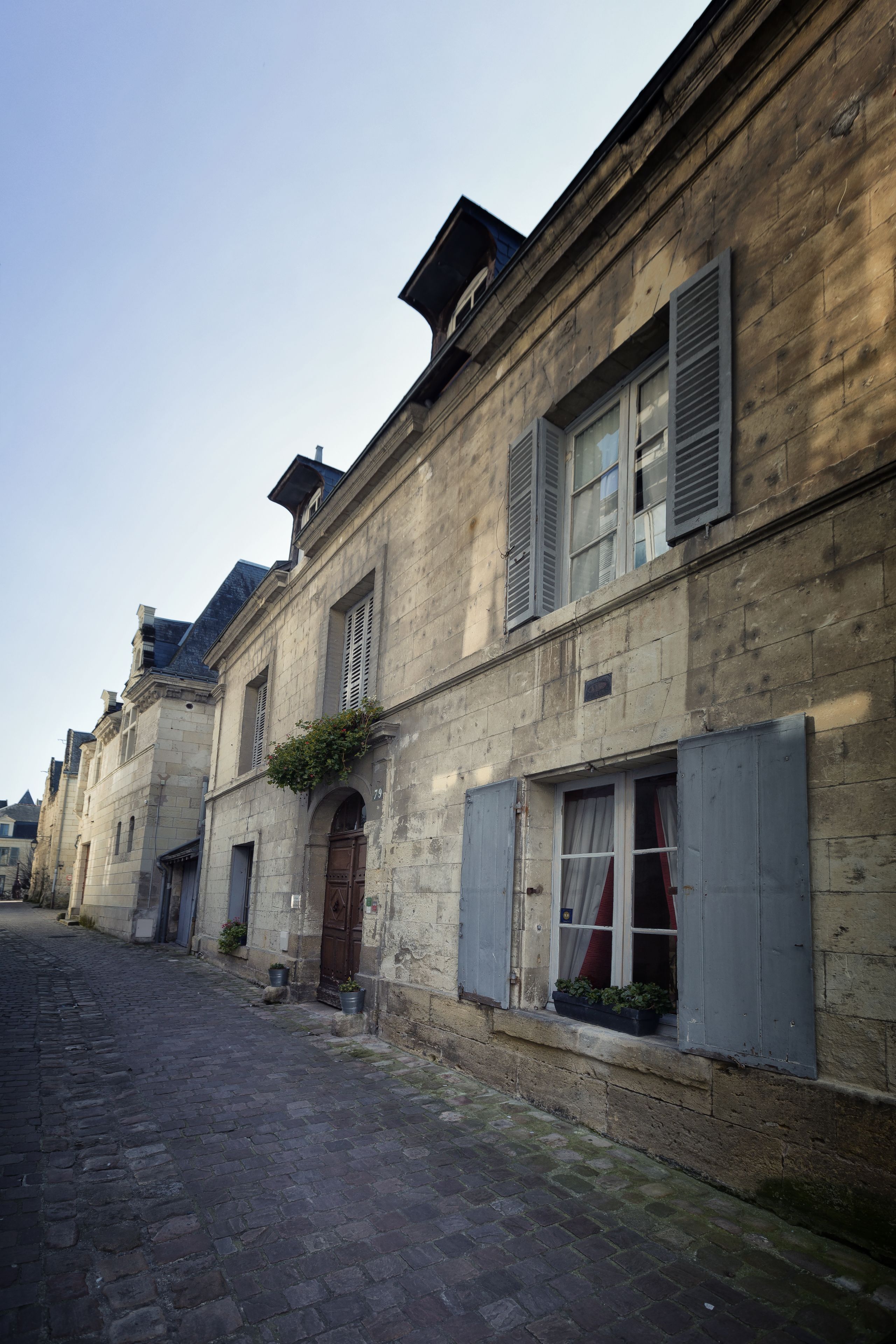 A narrow cobblestone street lined with historic stone buildings featuring shuttered windows and a central arched doorway.