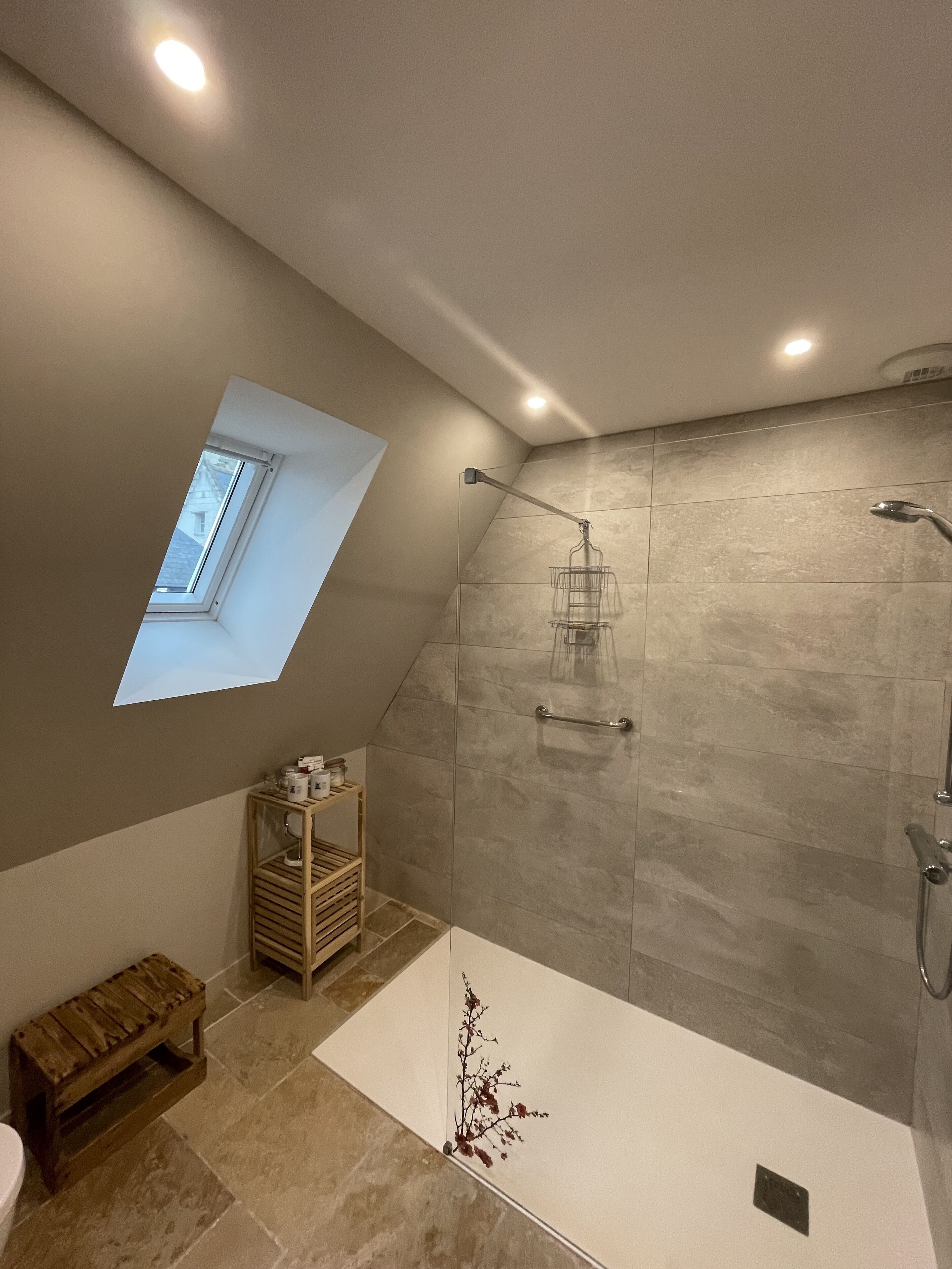 A modern bathroom with a skylight, a shower with a glass enclosure, and a wooden bench.