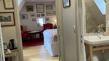 A hallway leading to a bedroom with a red chair, a bed with white bedding, and a bathroom with a sink and mirror.