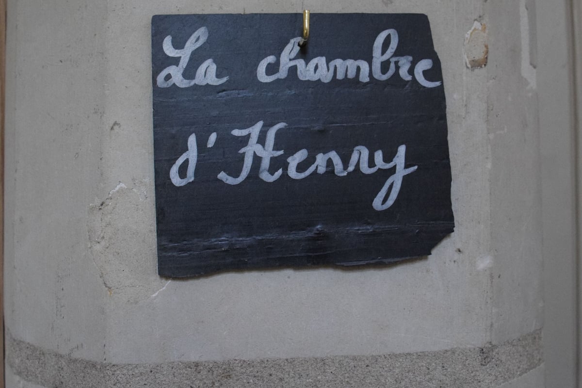 A black sign with white cursive text on a white wall.