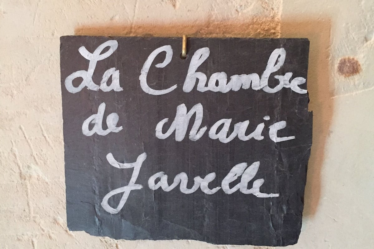 A black sign with white cursive writing on a textured beige wall.