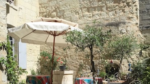 An outdoor patio with stone walls, metal chairs, tables with colorful tablecloths, and potted plants. - Au Relais Saint Maurice (Chinon)