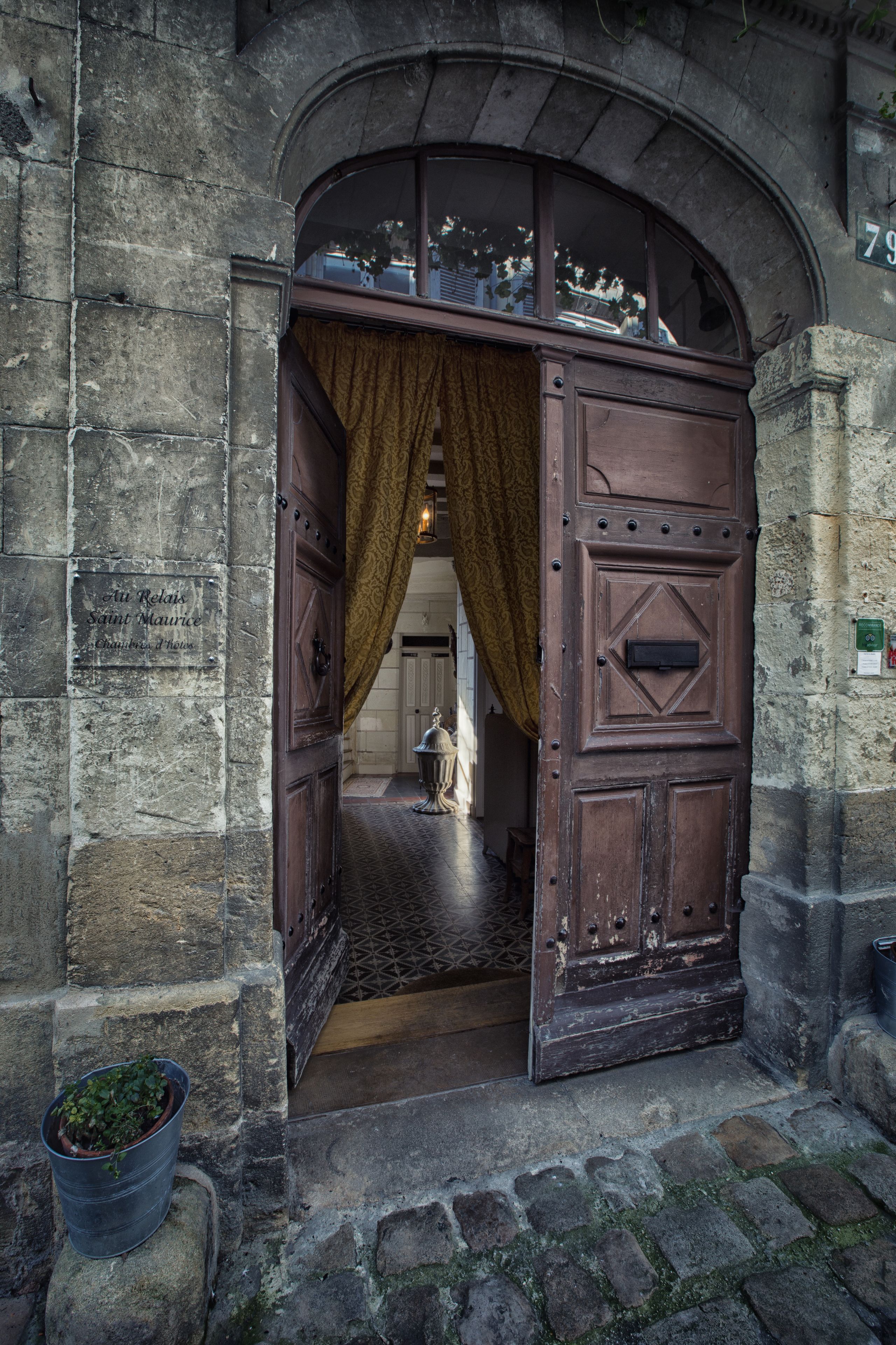 Un arco de entrada con una puerta de madera, una planta en maceta y un muro de piedra con una placa.