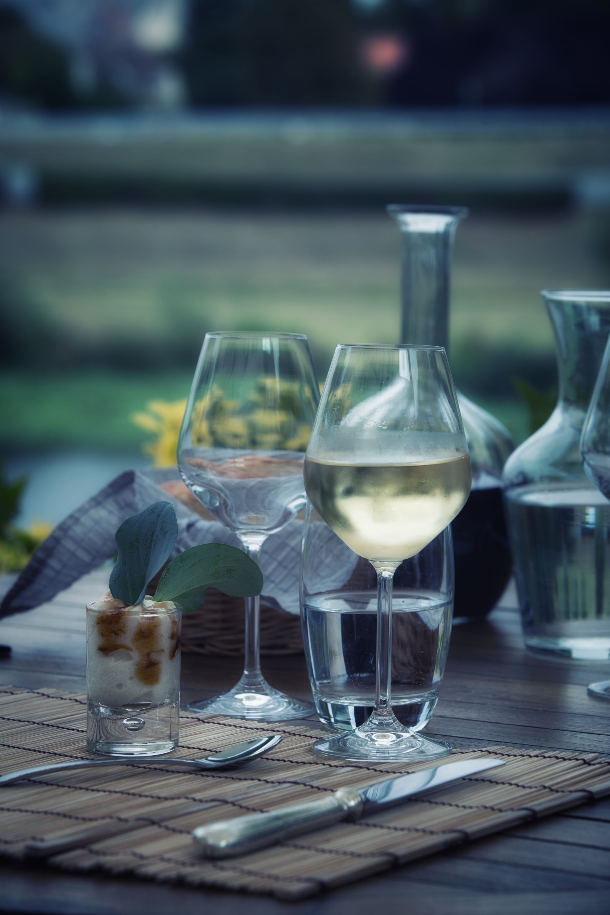A table with a glass of white wine, a small glass with a dessert, and a knife and spoon.