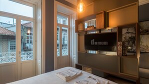Una habitación de hotel con una cama, dos ventanas, un televisor y una estantería decorativa.