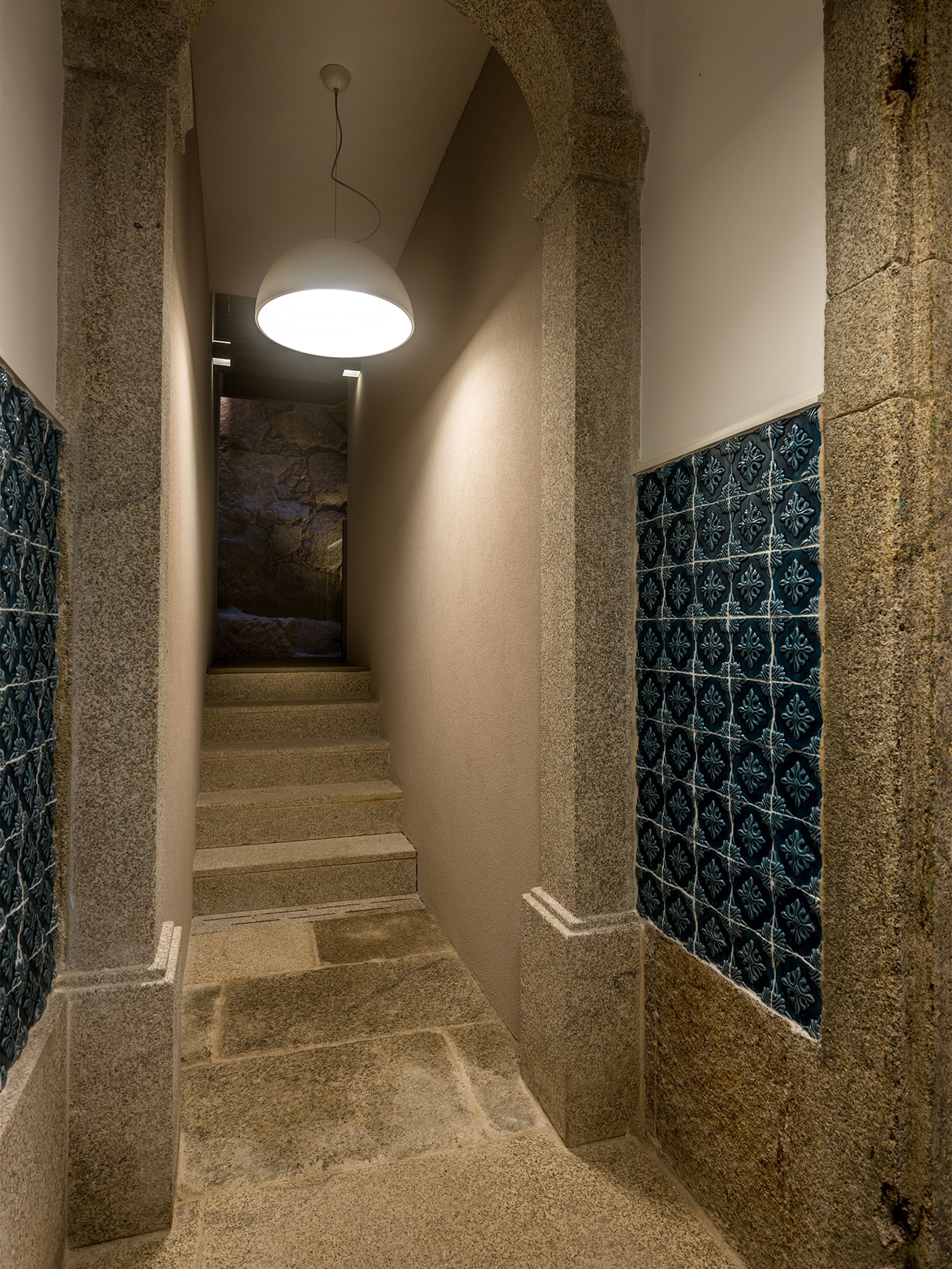 A stone staircase with a modern light fixture, leading to a room with patterned walls.