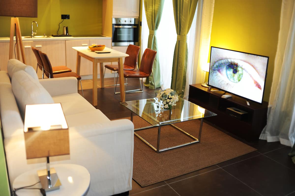 Una sala de estar moderna con un sofá, una mesa de centro de vidrio, un televisor y un comedor con sillas y una mesa.