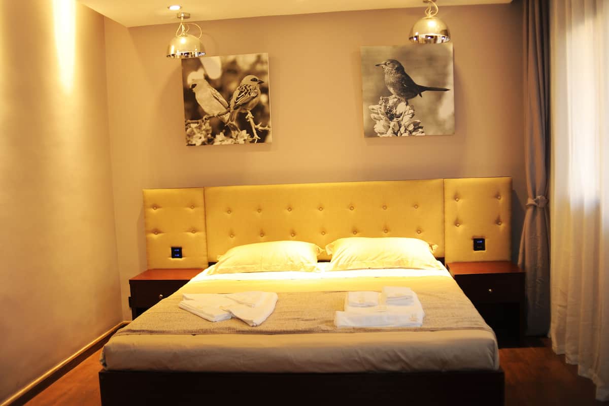 Una habitación de hotel con una cama grande, dos mesitas de noche y dos lámparas fijadas a la pared.