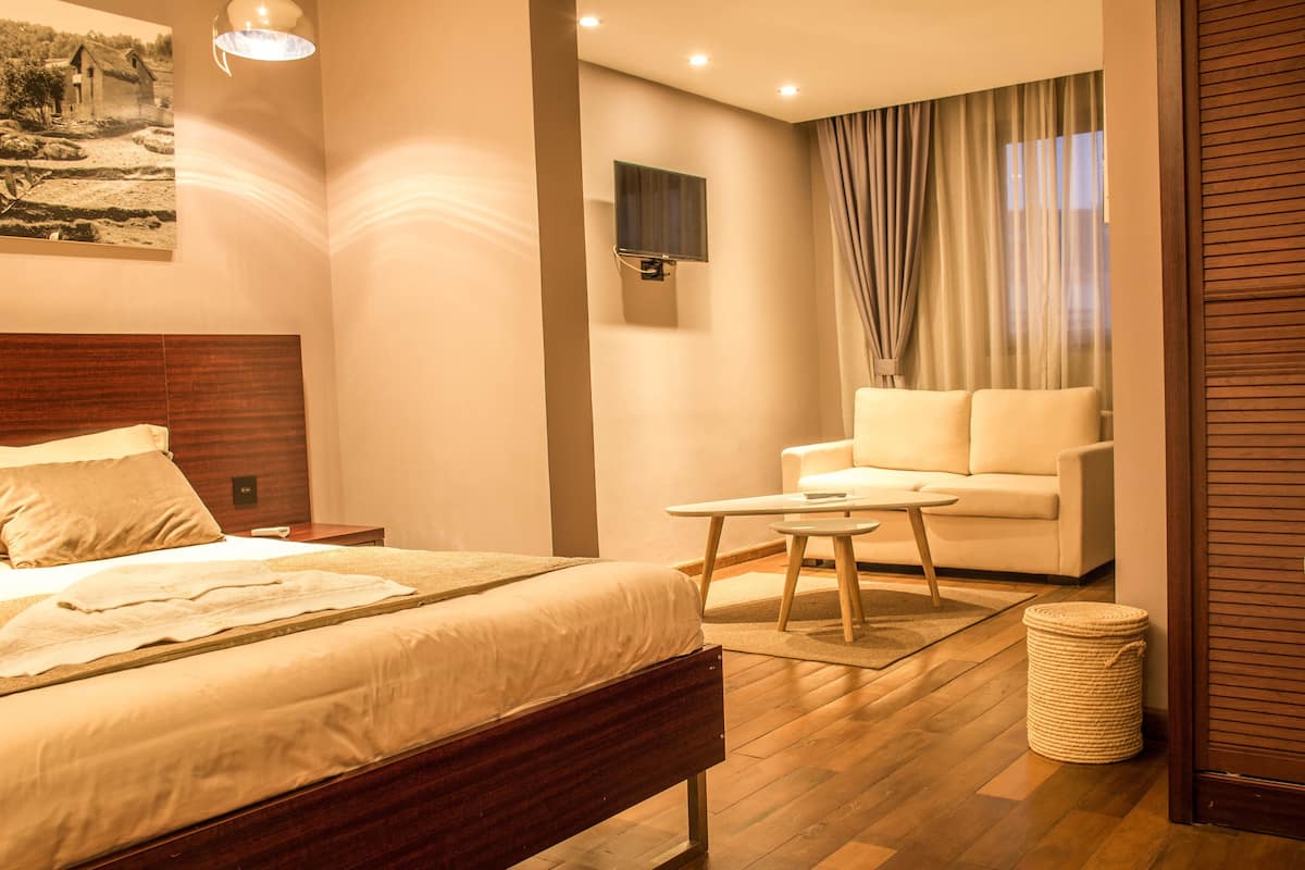 Habitación de hotel con cama, sofá, una mesita y televisor instalado en la pared.
