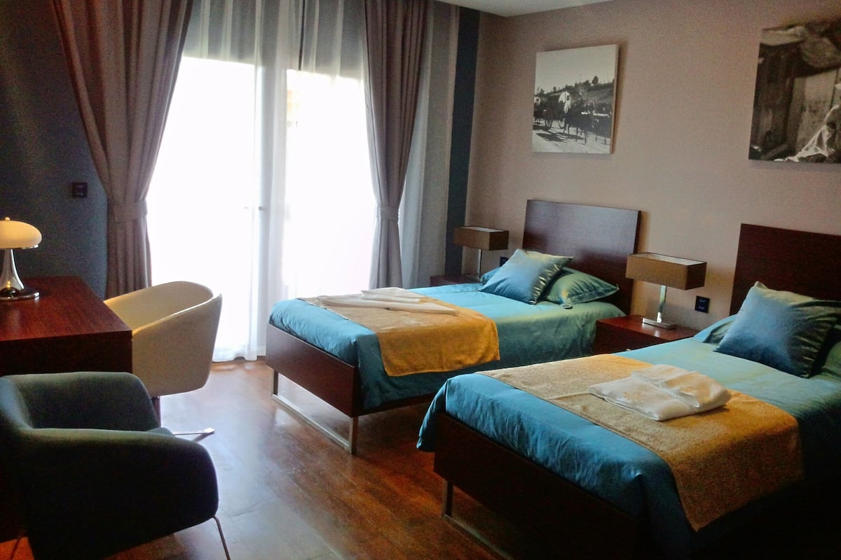 Habitación de hotel con dos camas, un escritorio, una silla y una ventana con cortinas.
