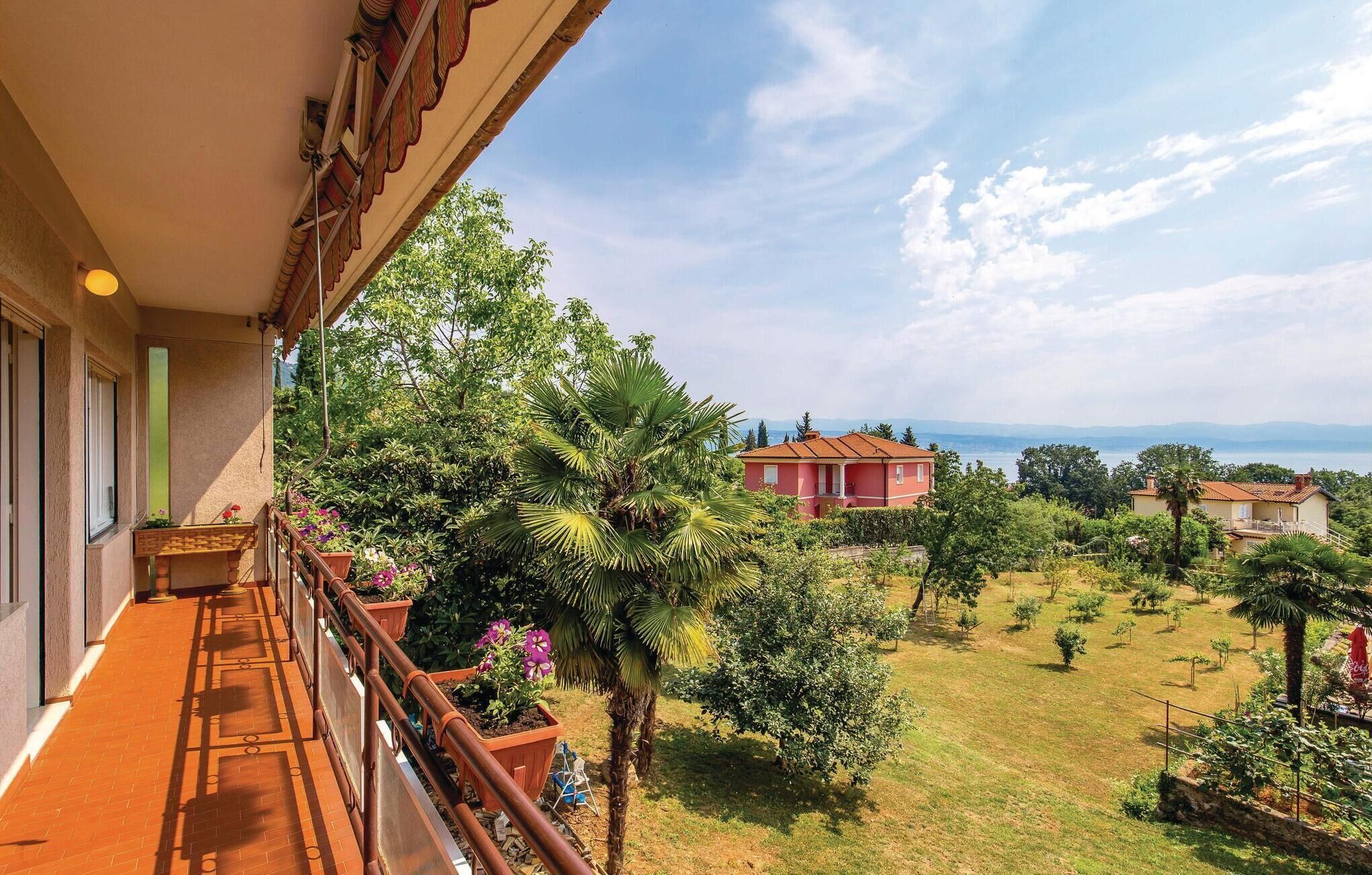 A balcony with a view of a lush garden and a distant red building.