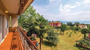 Un balcone con vista su un giardino rigoglioso e un edificio rosso in lontananza.