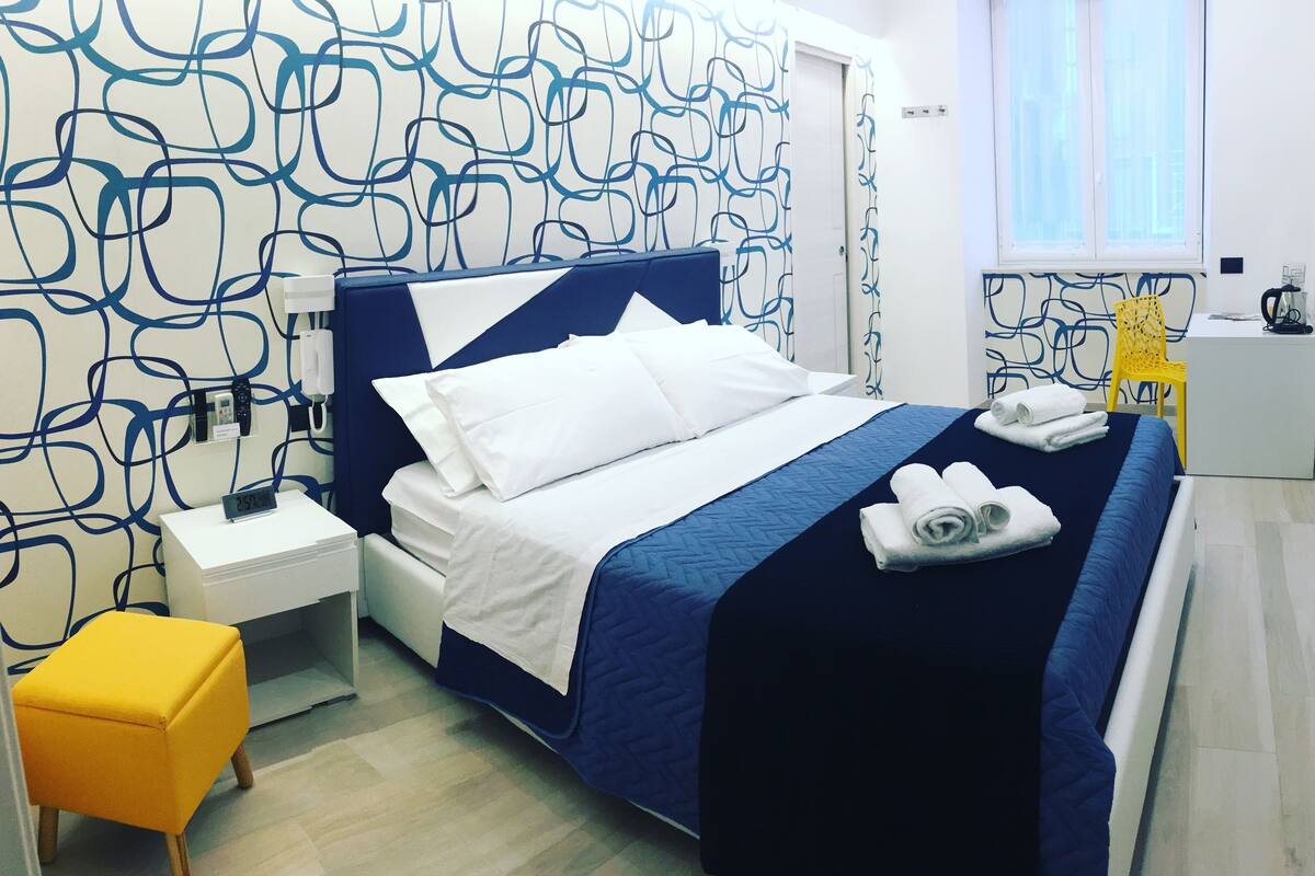 A hotel room with a bed, a small table, a chair, and a window.