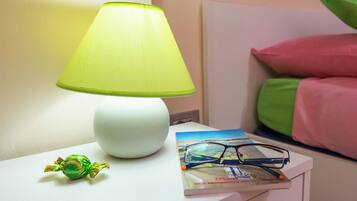 A bedside table with a white lamp, a book, glasses, and a wrapped candy.
