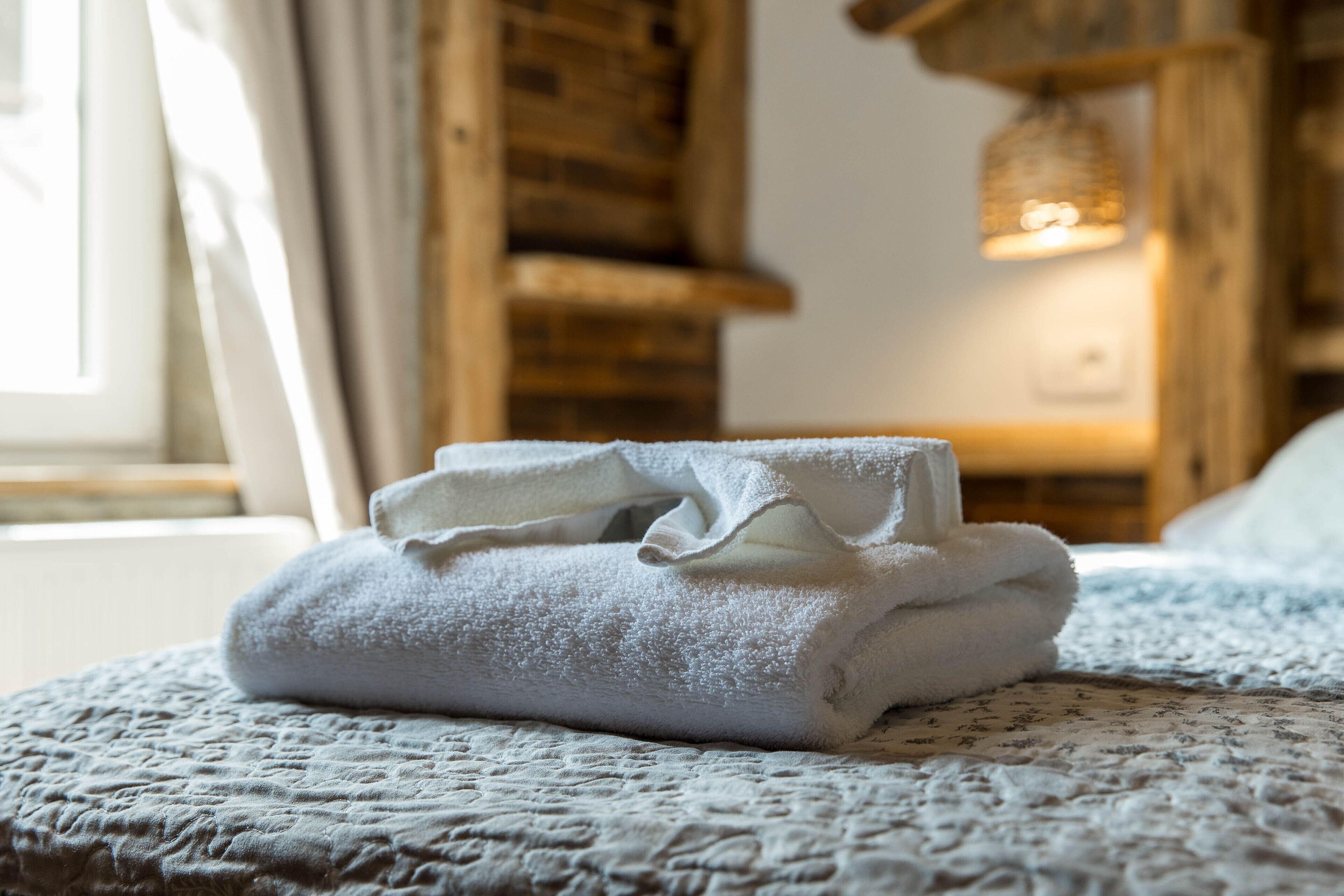 A neatly folded white towel on a textured bedspread in a room with wooden walls and a hanging light fixture.