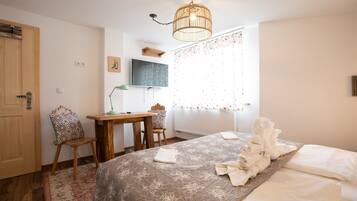 A bedroom with a bed, a desk, a chair, a television, and a window with curtains.