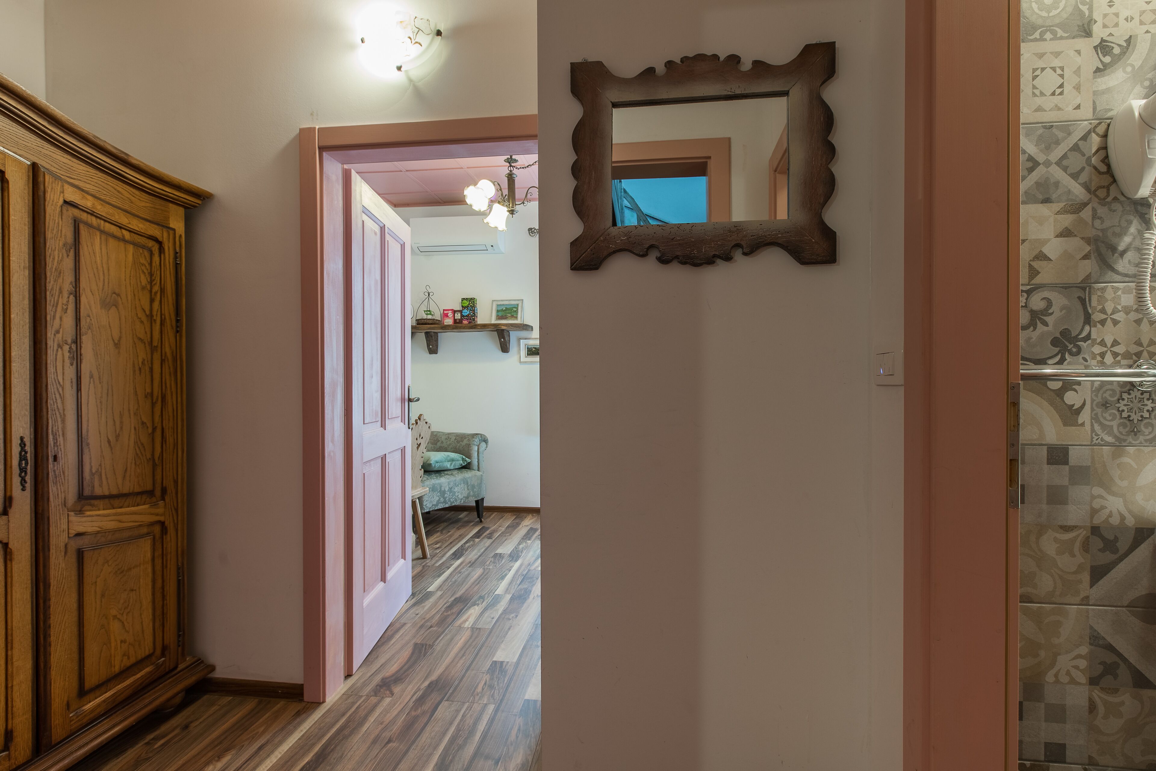 Un couloir avec une armoire en bois, une porte rose et un miroir accroché au mur.