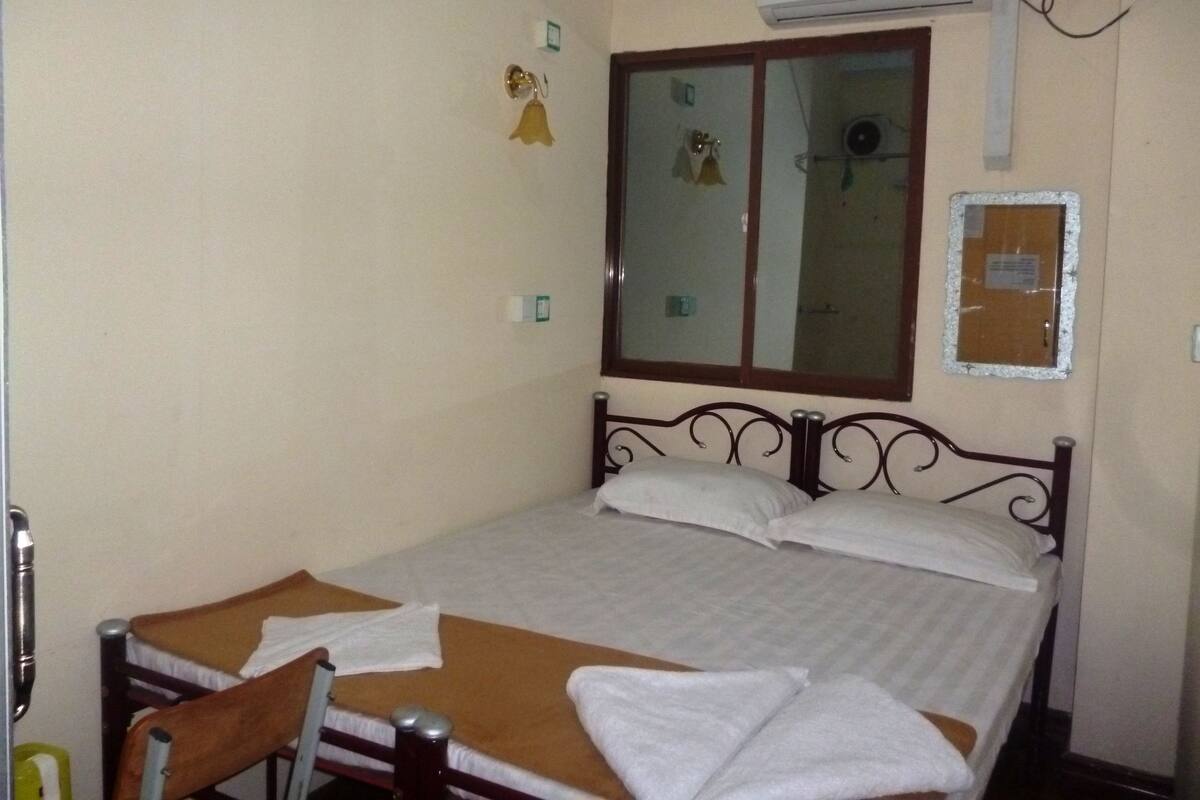 Una cama individual con estructura de madera, una ventana con vistas y un aire acondicionado instalado en la pared.
