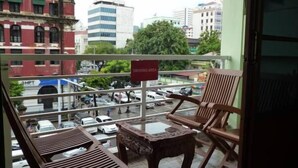 A balcony with wooden chairs and a small table, overlooking a busy street with cars and buildings. - Yangon Heart Guest House (Yangon)