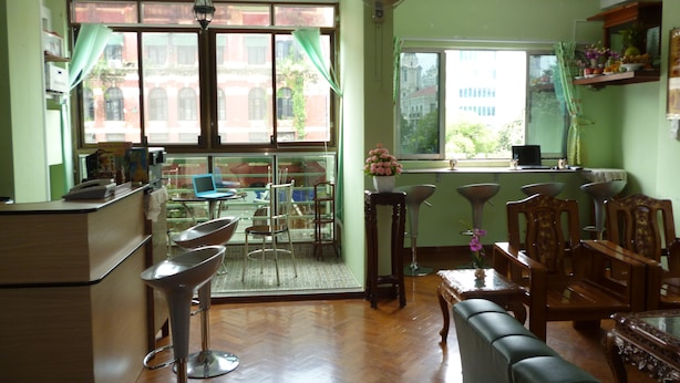 A room with a wooden floor, a dining table with chairs, a sofa, a small kitchen area, and large windows with curtains. - Yangon Heart Guest House (Yangon)