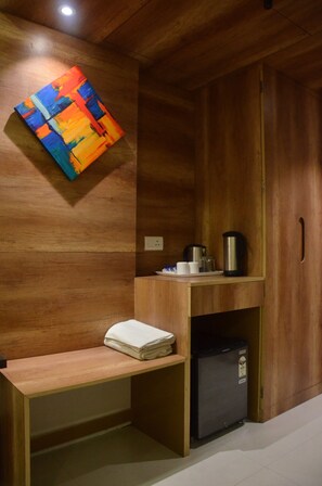 Quarto de madeira com uma mesa, um pequeno frigorífico e um quadro abstrato colorido na parede.