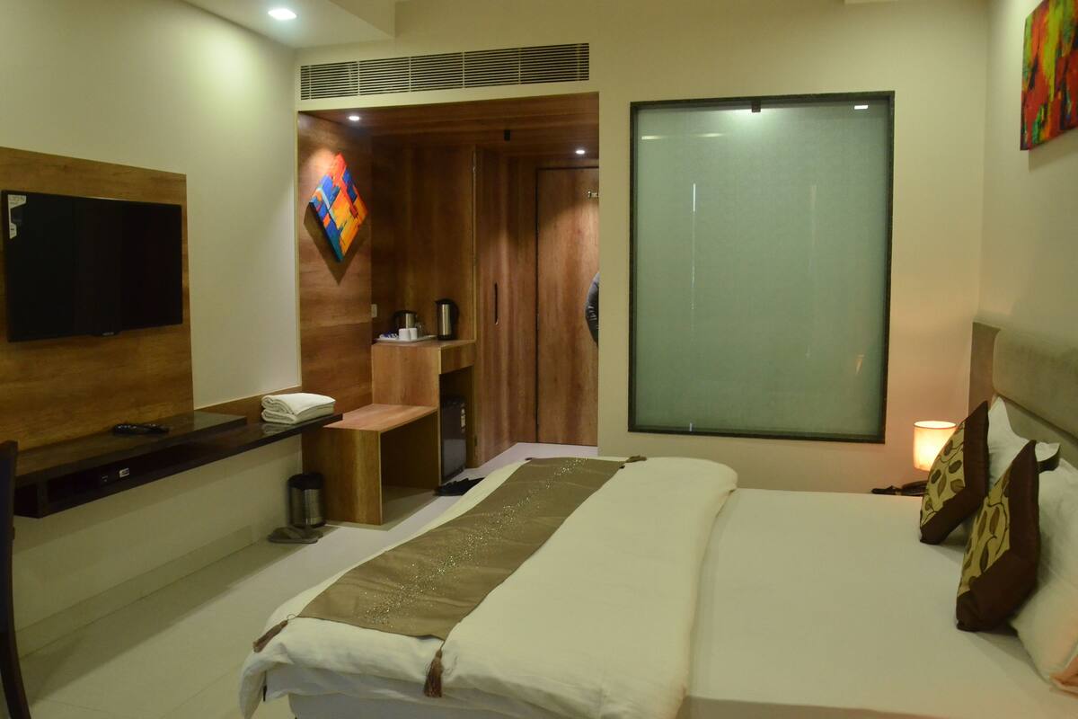 A hotel room with a bed, a desk, a TV, a window, and a shower area.
