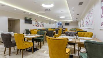 A dining area with multiple tables and chairs, a flat-screen TV mounted on the wall, and artwork on the walls.