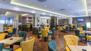 A spacious restaurant with yellow and green upholstered chairs, wooden tables, and a modern ceiling design. - Hotel Royal Inn (Belgrade)
