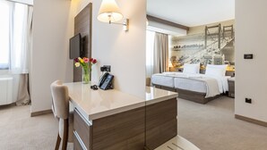 A hotel room with a desk, a phone, a vase with flowers, a bed, and a large window. - Hotel Royal Inn (Belgrade)