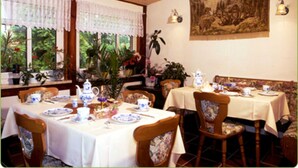 A dining area with tables set for tea service, chairs with floral upholstery, and a large painting on the wall. - Apartment - Pension Brilke (Ahrenshoop)