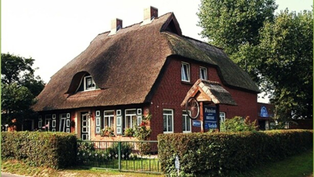 A traditional building with a thatched roof, a sign indicating a pub, and a brick facade. - Apartment - Pension Brilke (Ahrenshoop)