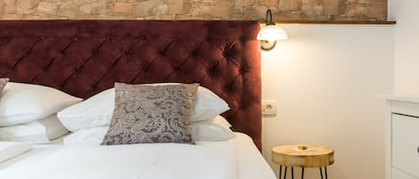 A bedroom with a stone wall, a tufted headboard, a bedside table, and a lamp.
