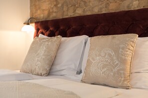 Una cama con pared de piedra de fondo y cabecera acolchada.